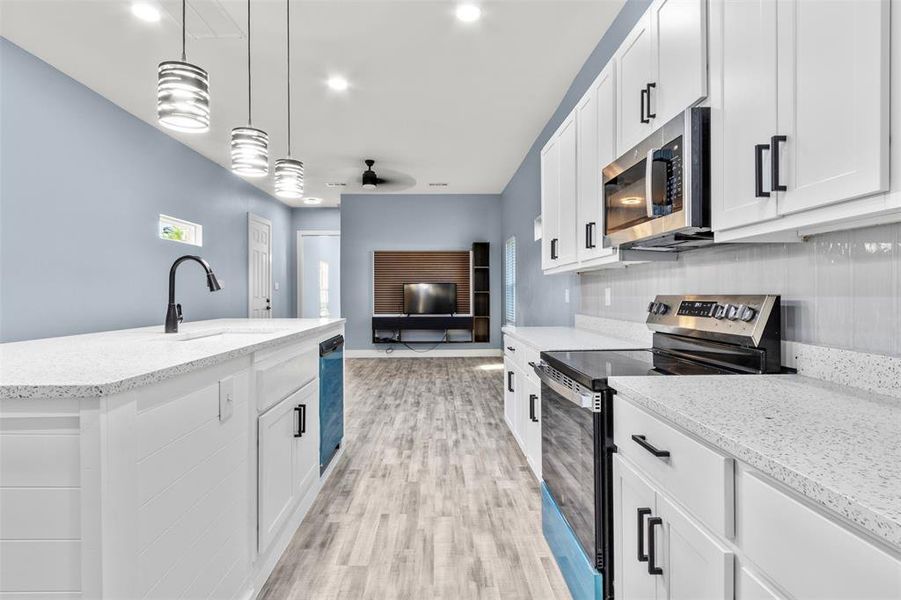 Kitchen with white cabinets, stainless steel appliances, sink, light hardwood / wood-style floors, and decorative light fixtures