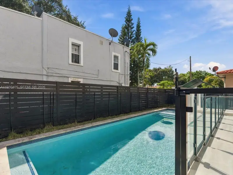 Rectangular swimming pool featuring a tile border, complemented by a horizontal slat privacy fence and a glass panel safety railing Rectangular swimming pool featuring a tile border, complemented by a horizontal slat privacy fence and a glass panel safety railing