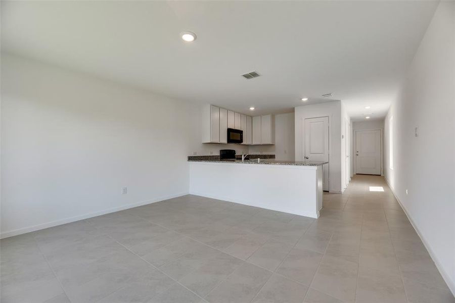 Kitchen featuring light tile patterned floors, sink, kitchen peninsula, stone counters, and white cabinetry