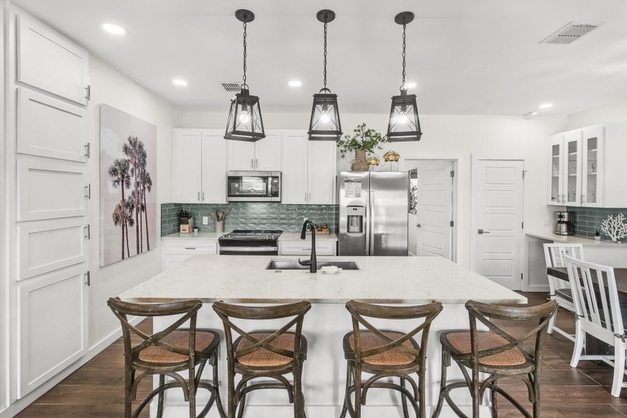 Kitchen with decorative backsplash, glass insert cabinets, decorative light fixtures, a kitchen bar, and stainless steel appliances Kitchen with decorative backsplash, glass insert cabinets, decorative light fixtures, a kitchen bar, and stainless steel appliances