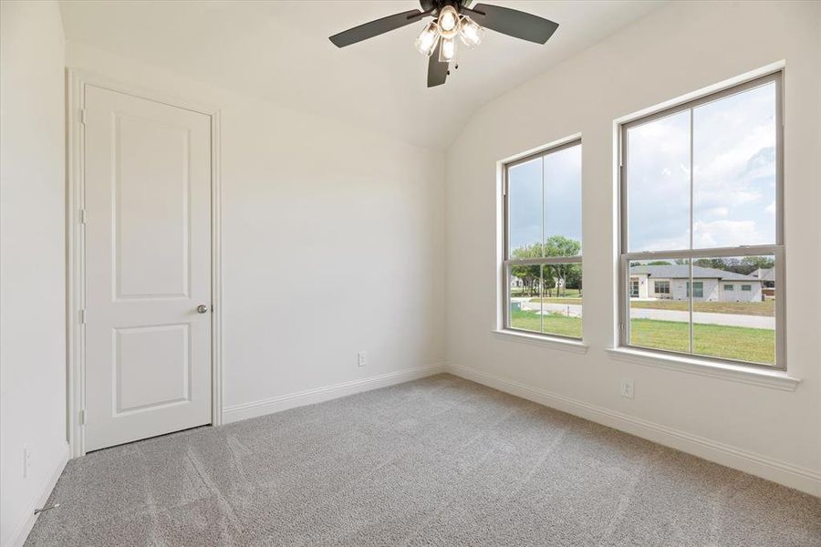 Empty room with lofted ceiling, carpet flooring, and ceiling fan