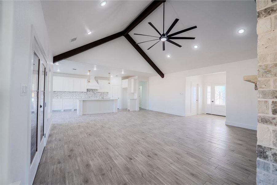Unfurnished living room with beamed ceiling, a ceiling fan, light wood finished floors, high vaulted ceiling, and recessed lighting Unfurnished living room with beamed ceiling, a ceiling fan, light wood finished floors, high vaulted ceiling, and recessed lighting