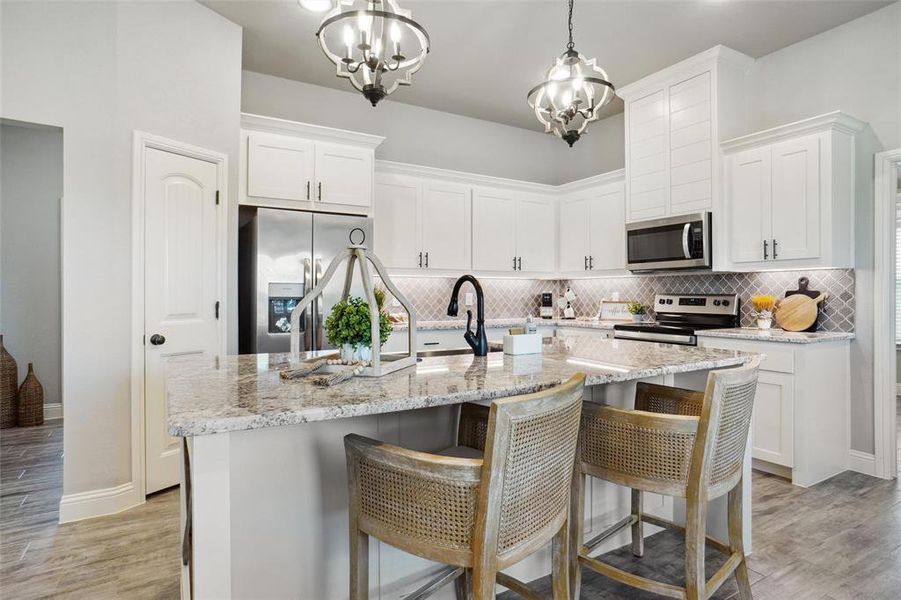 Kitchen featuring appliances with stainless steel finishes, an island with sink, light hardwood / wood-style flooring, and decorative backsplash