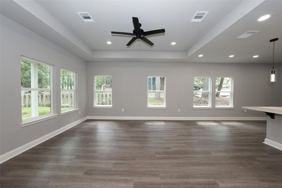 This spacious living room is filled with natural light from large windows that overlook the backyard patio and wooded backyard. A ceiling fan adds comfort, while the open layout creates a welcoming space for relaxation and entertaining.