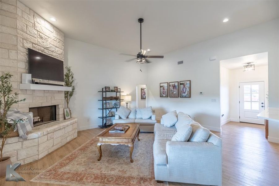 Living room with wood finished floors, a stone fireplace, a ceiling fan, and recessed lighting Living room with wood finished floors, a stone fireplace, a ceiling fan, and recessed lighting