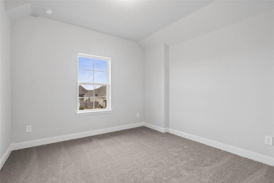 The secondary bedroom offers a bright and airy atmosphere neutral walls, lighting, plush carpet flooring, and a large window that fills the space with natural light.