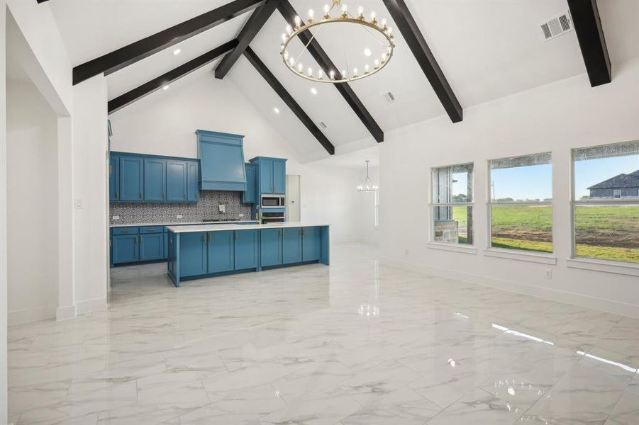 Kitchen featuring backsplash, high vaulted ceiling, blue cabinetry, appliances with stainless steel finishes, and a notable chandelier