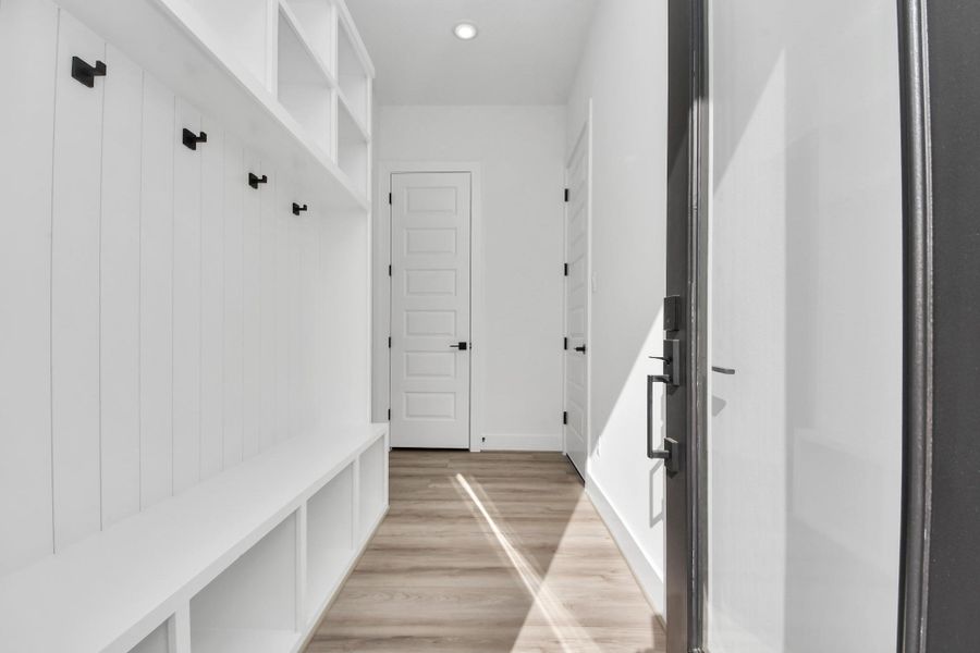 This photo showcases a bright, modern mudroom with white walls, built-in storage cubbies, and hooks for organization. The space features a sleek design with light wood flooring and ample natural light.