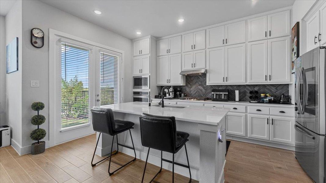Kitchen with wood finish floors, stainless steel appliances, white cabinets, backsplash, and recessed lighting Kitchen with wood finish floors, stainless steel appliances, white cabinets, backsplash, and recessed lighting
