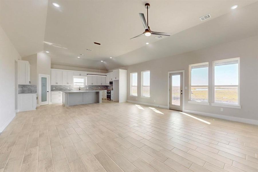 Unfurnished living room featuring visible vents, lofted ceiling, ceiling fan, and light wood-style flooring