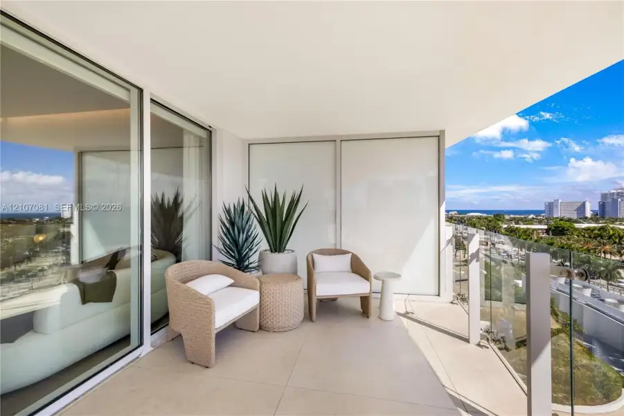 Covered balcony featuring large-format stone flooring, glass panel railings, and floor-to-ceiling sliding glass doors Covered balcony featuring large-format stone flooring, glass panel railings, and floor-to-ceiling sliding glass doors