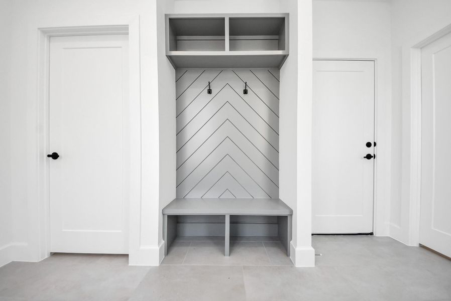 A smart mudroom solution tailored for modern lifestyles, complete with a built-in bench, chevron-detail backdrop, hanging hooks, and open shelving—designed for seamless organization and daily ease.