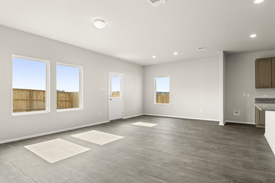 Image of a living room with dark vinyl flooring, light grey walls and windows with a white back door