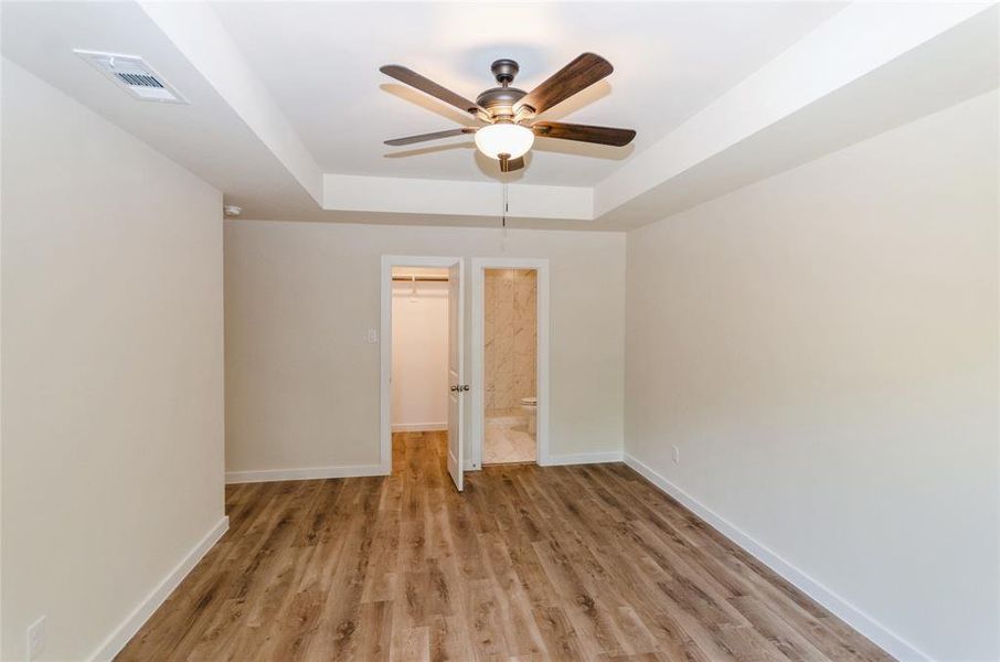 Unfurnished bedroom with ceiling fan, light hardwood / wood-style flooring, a raised ceiling, and a walk in closet