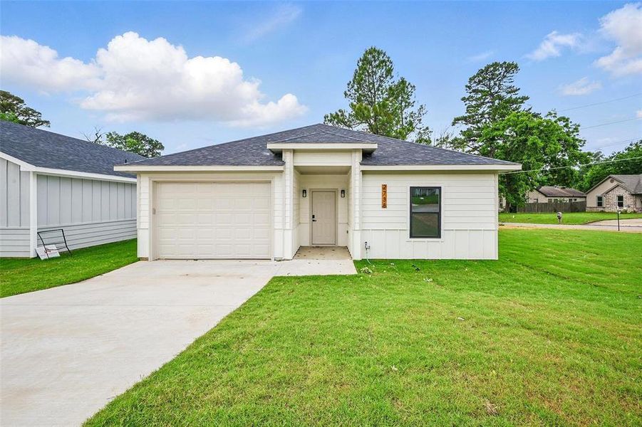 View of front facade featuring a front lawn, driveway, an attached garage, and a shingled roof