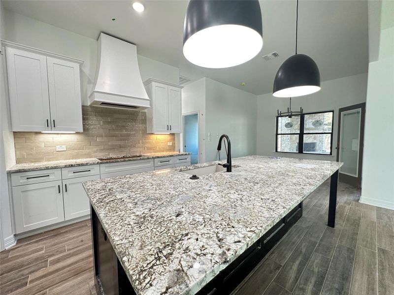 Kitchen featuring wood finish floors, light stone countertops, white cabinets, custom exhaust hood, and backsplash