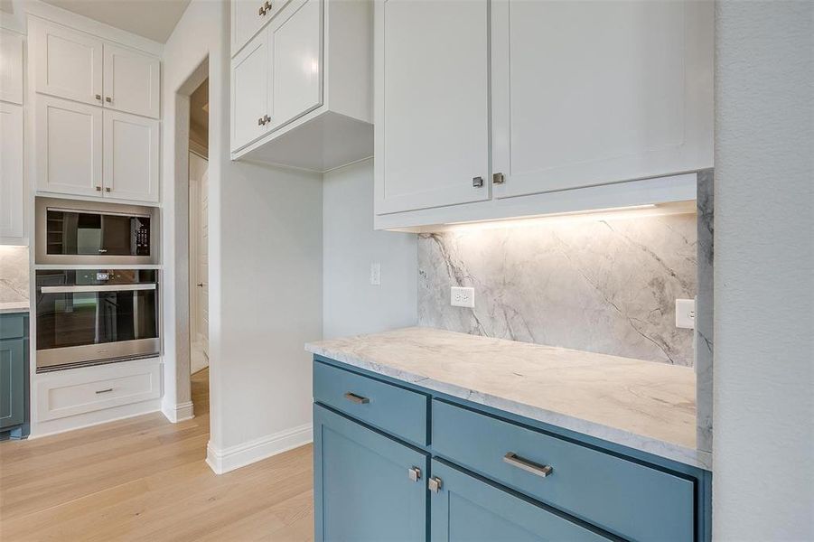 Kitchen with backsplash, appliances with stainless steel finishes, light hardwood / wood-style flooring, and white cabinetry