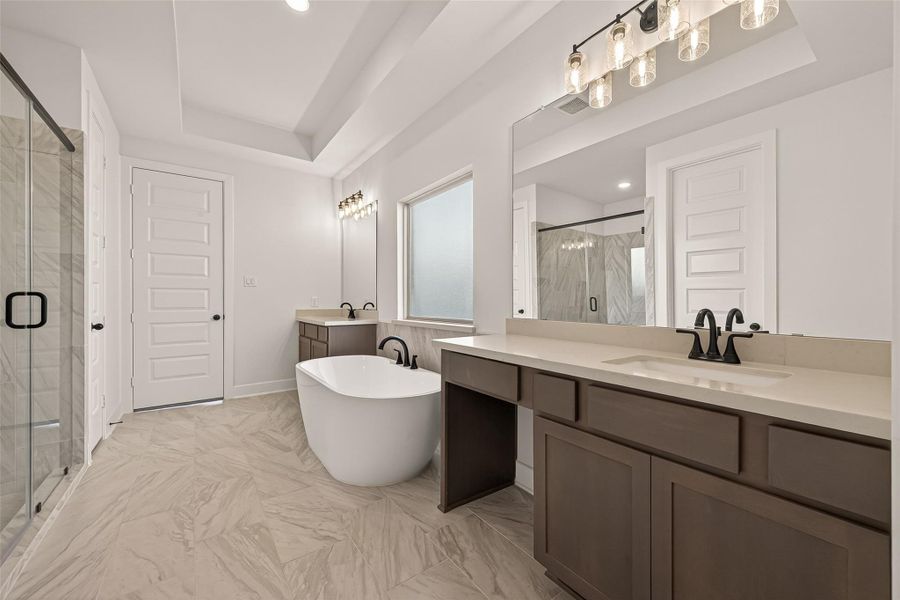 This spacious bathroom features a modern freestanding tub, dual vanities with sleek black fixtures, and a large glass-enclosed shower. The neutral tones and ample lighting cre