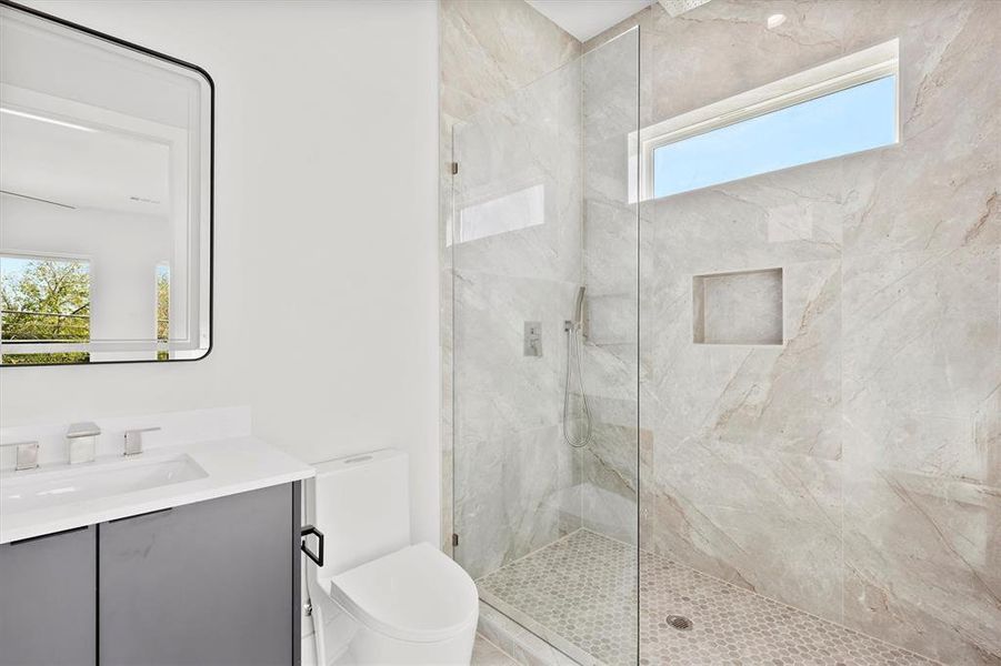 Bathroom with vanity, a healthy amount of sunlight, a tile shower, and toilet