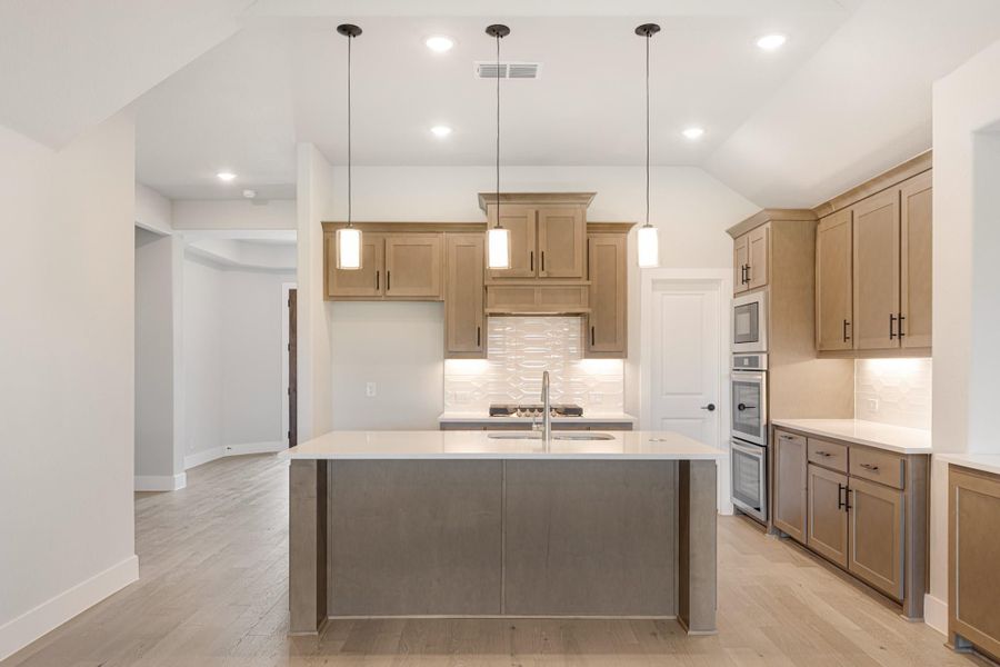 Kitchen with large center island, tan wood cabinets, white countertops, and pendant lights over the island Kitchen with large center island, tan wood cabinets, white countertops, and pendant lights over the island
