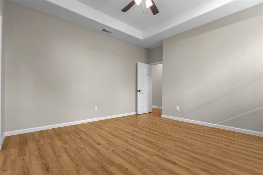 Unfurnished room with a tray ceiling, light wood-style flooring, and ceiling fan