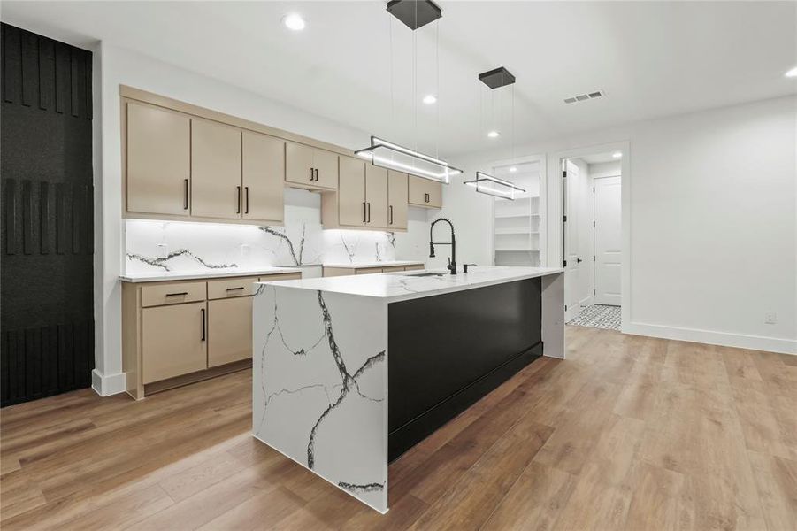 Kitchen with decorative light fixtures, light stone countertops, cream cabinetry, recessed lighting, and decorative backsplash Kitchen with decorative light fixtures, light stone countertops, cream cabinetry, recessed lighting, and decorative backsplash