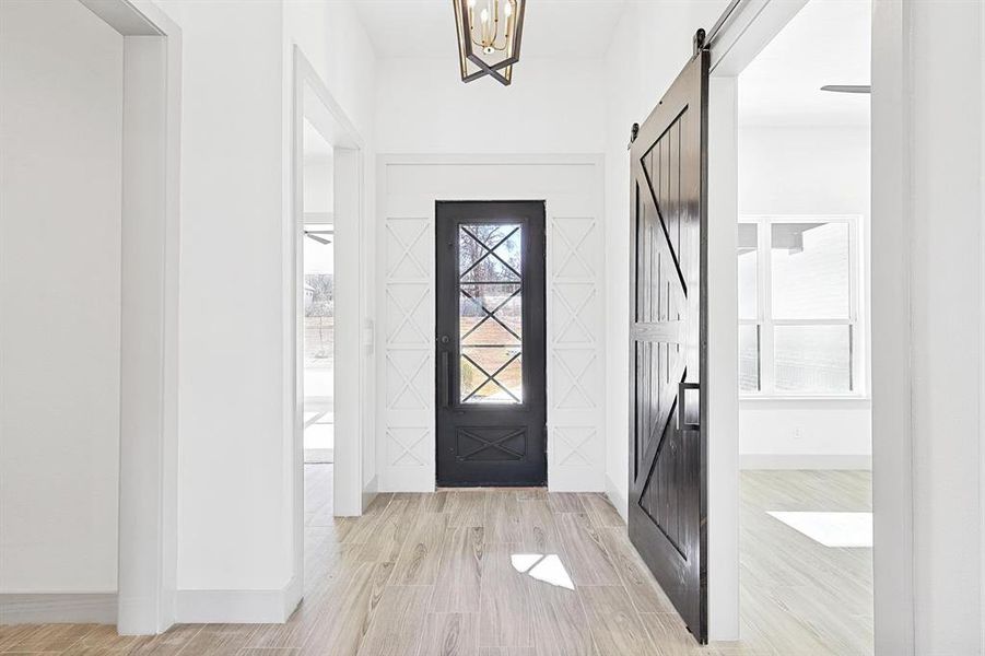 Foyer entrance featuring a barn door, light wood-style flooring, and a chandelier Foyer entrance featuring a barn door, light wood-style flooring, and a chandelier