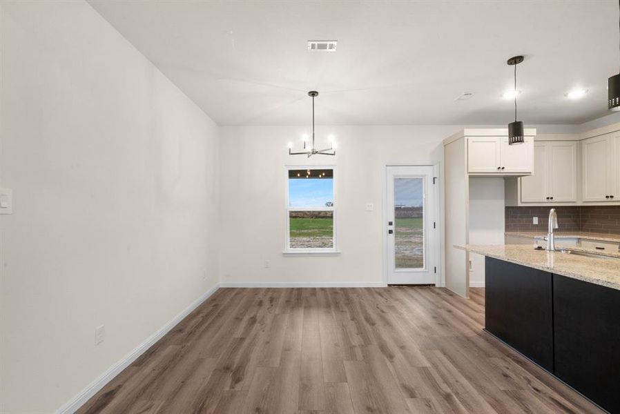 Kitchen featuring an inviting chandelier, white cabinets, hanging light fixtures, decorative backsplash, and light stone counters Kitchen featuring an inviting chandelier, white cabinets, hanging light fixtures, decorative backsplash, and light stone counters