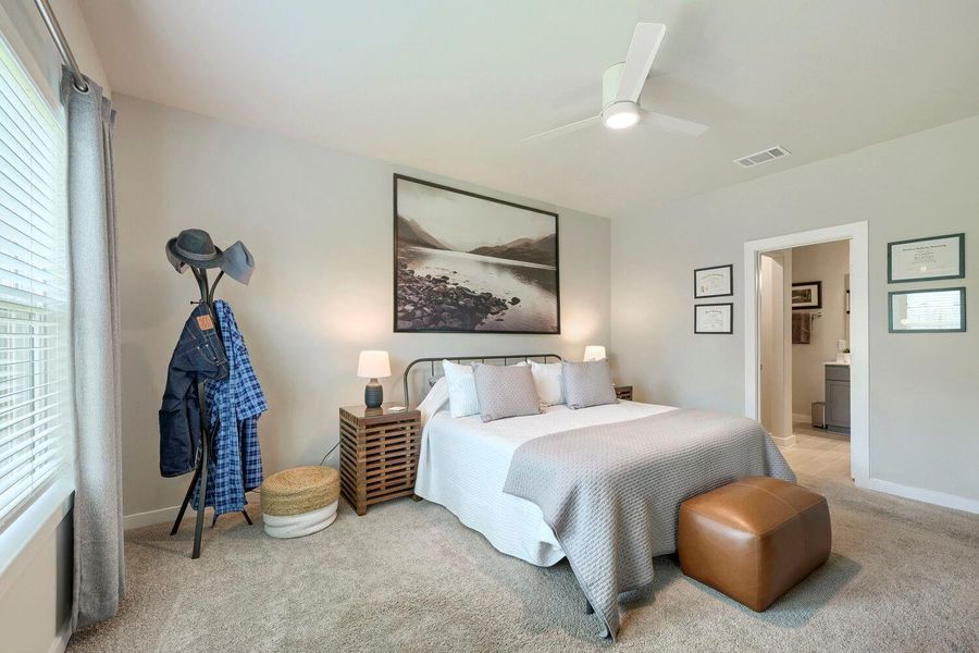 A well-lit bedroom features plush carpeting, a modern ceiling fan, and direct access to a private bathroom. A well-lit bedroom features plush carpeting, a modern ceiling fan, and direct access to a private bathroom.