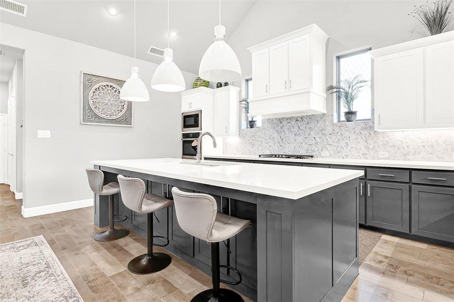 Kitchen with backsplash, decorative light fixtures, a breakfast bar area, light wood-type flooring, and lofted ceiling
