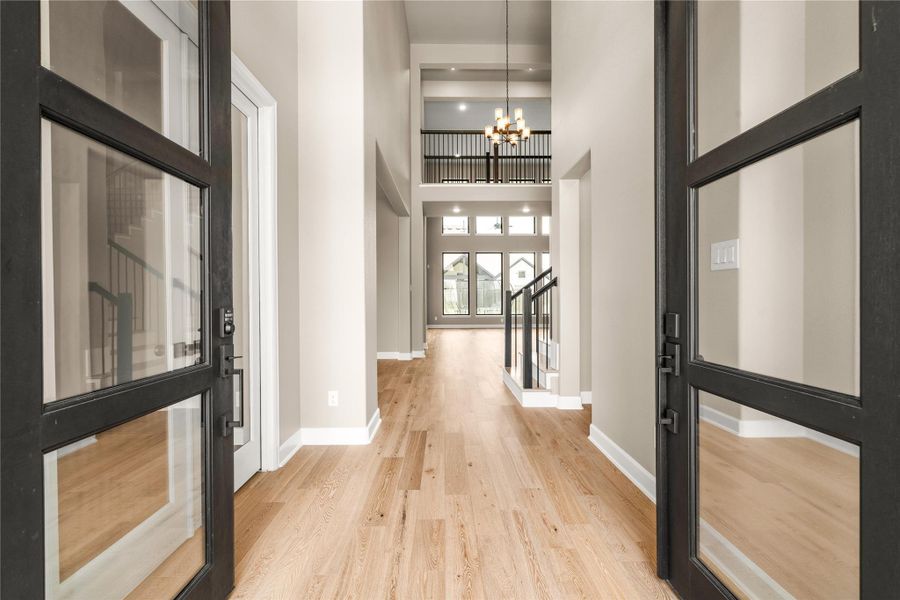 Elegant entryway with high ceilings, abundant natural light, and a view through to the spacious open living area, highlighted by a modern chandelier and sleek staircase.