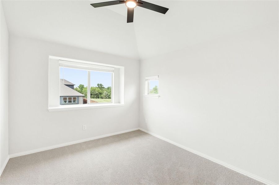 Empty bedroom with vaulted ceiling, ceiling fan, carpet flooring, and two windows with natural light