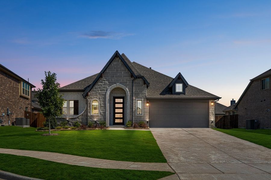 Single-story stone home with arched entry, two-car garage, and manicured lawn at dusk