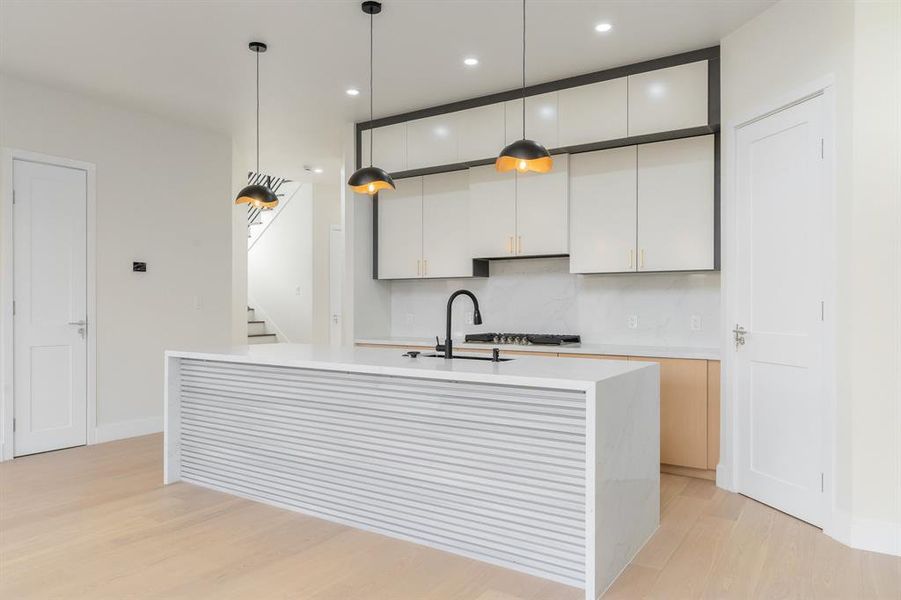 Kitchen featuring hanging light fixtures, white cabinetry, light wood-style flooring, light stone counters, and a kitchen island with sink Kitchen featuring hanging light fixtures, white cabinetry, light wood-style flooring, light stone counters, and a kitchen island with sink