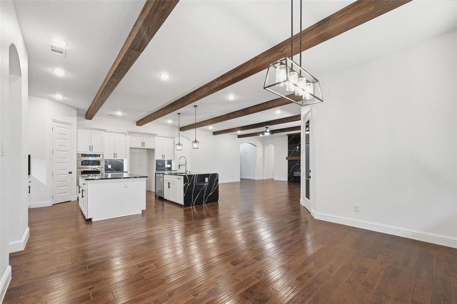 Kitchen with arched walkways, hanging light fixtures, open floor plan, a center island with sink, and beam ceiling