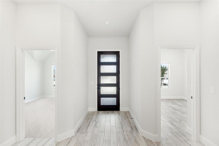 Bright entryway with black glass-panel front door, white walls, and light wood-look tile floors