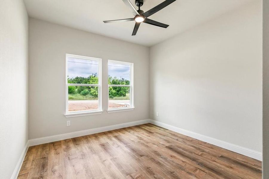 Spacious room featuring two windows, wood-finish flooring, white baseboards, light neutral wall paint, and a contemporary ceiling fan with integrated lighting