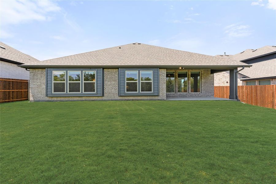 Rear exterior of single-story brick home with large windows, covered patio, and fenced backyard lawn. Rear exterior of single-story brick home with large windows, covered patio, and fenced backyard lawn.