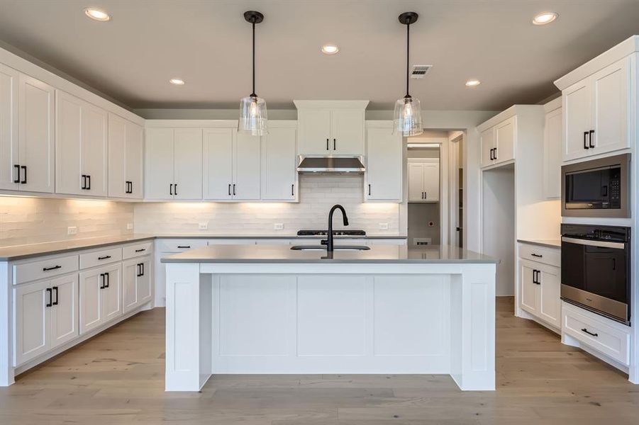 Kitchen featuring oven, under cabinet range hood, built in microwave, a sink, and an island with sink Kitchen featuring oven, under cabinet range hood, built in microwave, a sink, and an island with sink