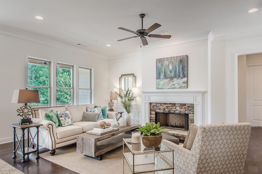 Living room with dark wood-style flooring, ornamental molding, recessed lighting, a stone fireplace, and a ceiling fan Living room with dark wood-style flooring, ornamental molding, recessed lighting, a stone fireplace, and a ceiling fan