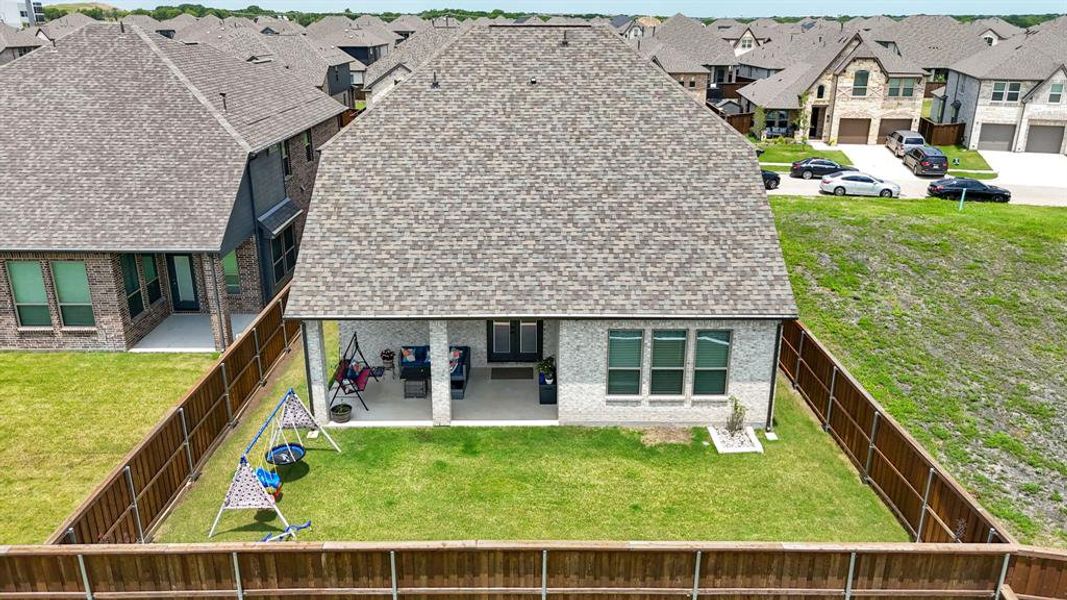 Rear exterior featuring a covered patio, a fenced backyard with a grass lawn, and a light-colored brick facade with dark framed windows Rear exterior featuring a covered patio, a fenced backyard with a grass lawn, and a light-colored brick facade with dark framed windows