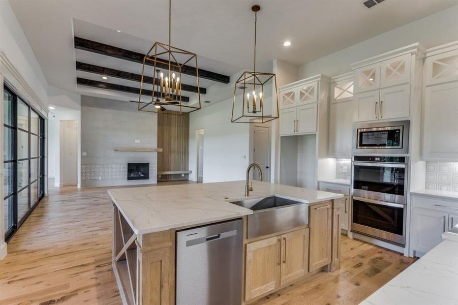 Kitchen featuring an island with sink, beamed ceiling, stainless steel appliances, sink, and a notable chandelier