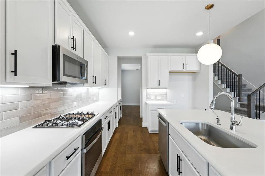 Stylish and sleek kitchen with modern lighting, wood floors, white cabinets and light countertops with gas cooktop and SS appliances.