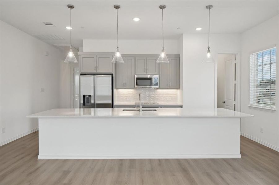 Kitchen with gray cabinets, a spacious island, sink, and stainless steel appliances