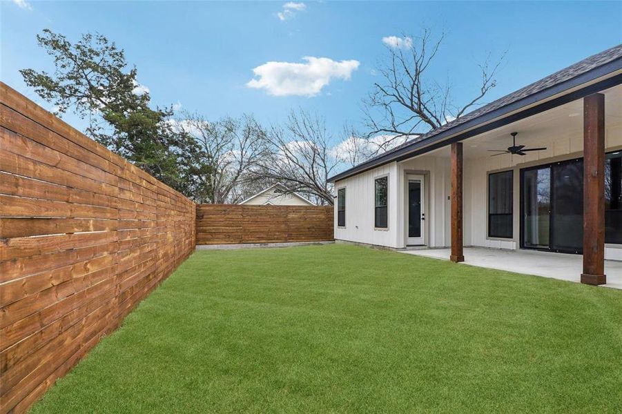 The property features a spacious lawn area, a privacy fence, and a covered patio with a ceiling fan