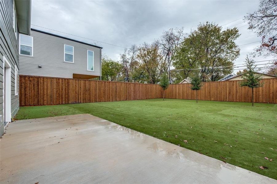 Fenced backyard featuring a large patio and synthetic turf lawn