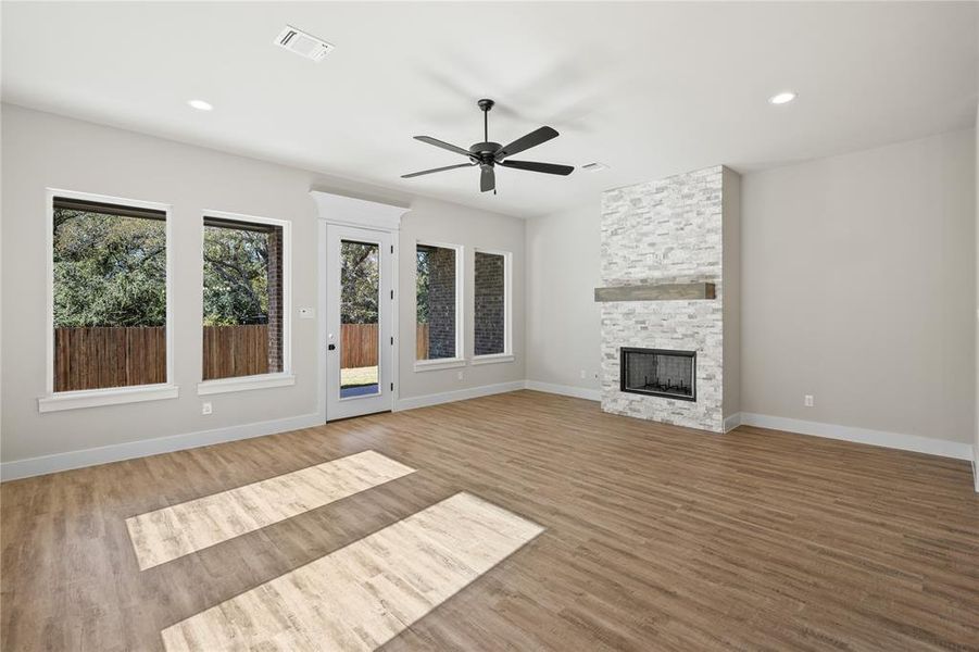 Unfurnished living room with light wood-style flooring, a ceiling fan, a stone fireplace, and recessed lighting