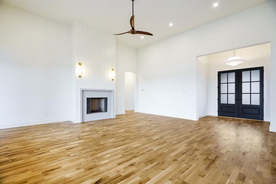 Unfurnished living room featuring a high ceiling, light hardwood / wood-style flooring, french doors, and ceiling fan