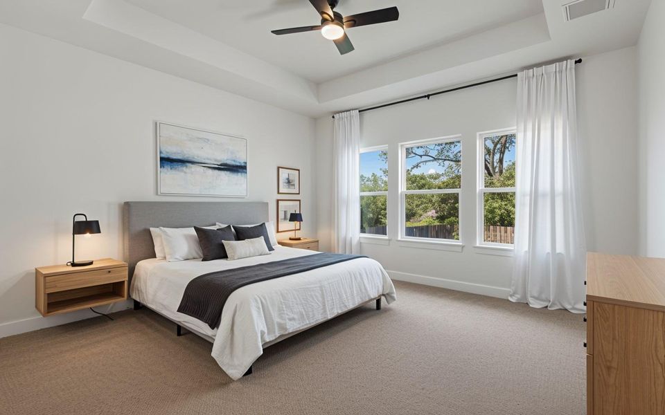 Spacious bedroom with a tray ceiling and recessed lighting, featuring plush carpet flooring and multiple windows( Ai staging)