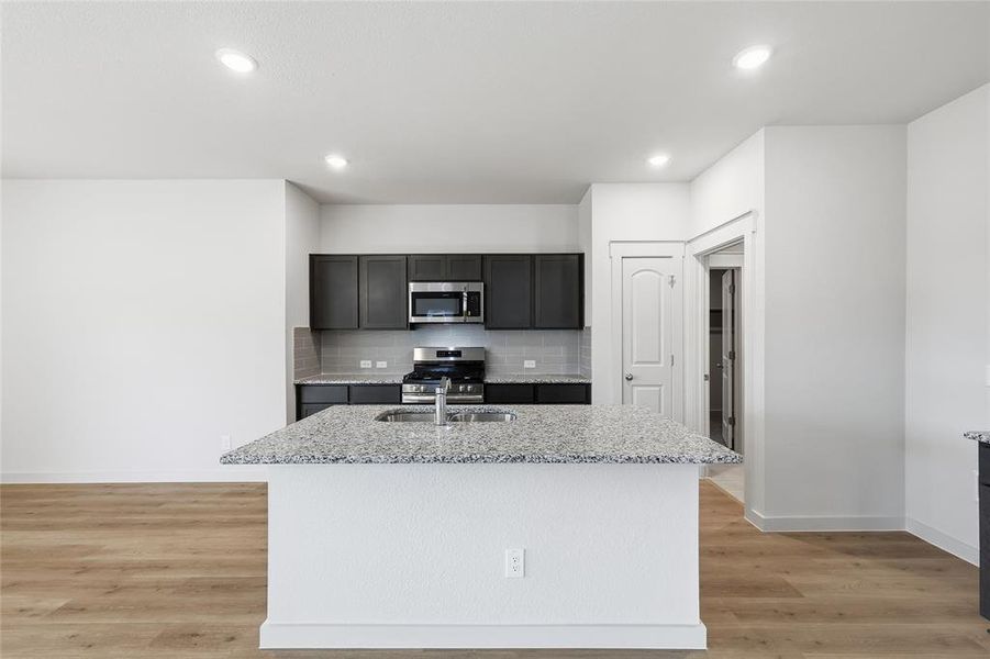 Kitchen with decorative backsplash, light stone countertops, a center island with sink, appliances with stainless steel finishes, and recessed lighting